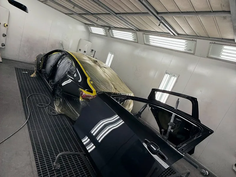 Black sedan in paint booth with fresh coat